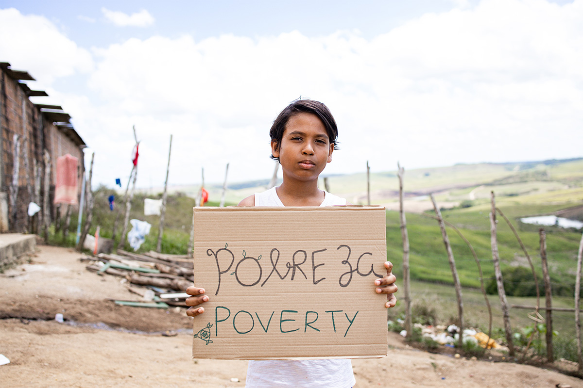 A boy holds a sign that says "poverty"