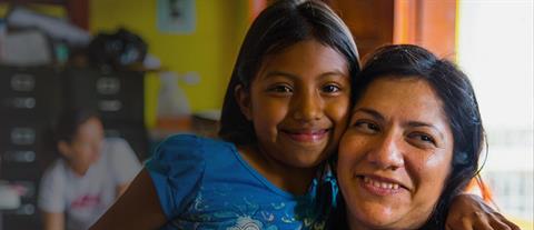 A young girl in a cheek to cheek hug with an adult woman