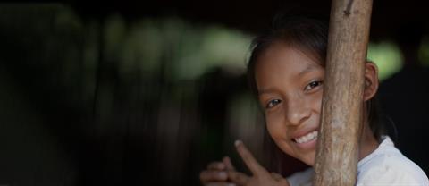 A girl smiling behind a wooden post