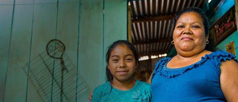 A woman in blue has her arm around a young girl wearing teal