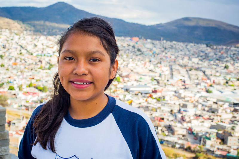 A girl stands in front of her city and smiles