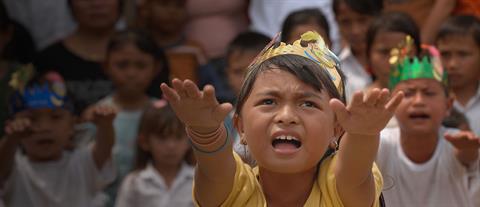 A young girl wearing a paper crown stretches her arms out in front of her