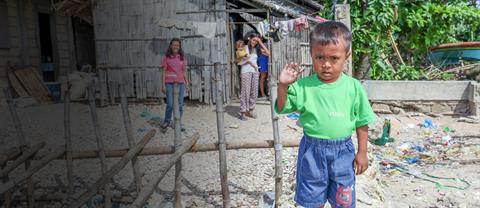 A young boy standing outside and waving