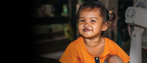 A little girl in an orange shirt sits on the floor and smiles