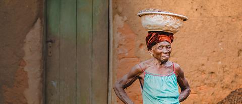 A elderly woman balances a basket on her head