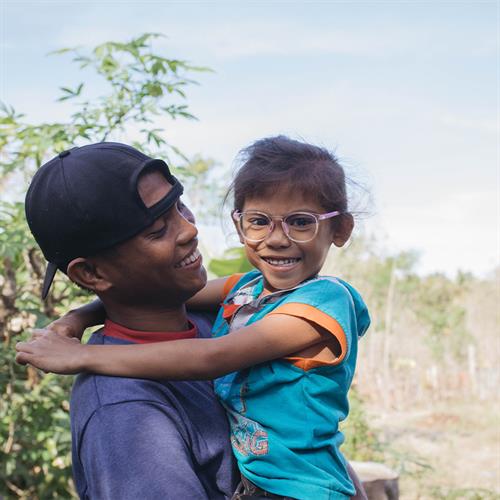 Man holds child in teal shirt with glasses. She smiles.