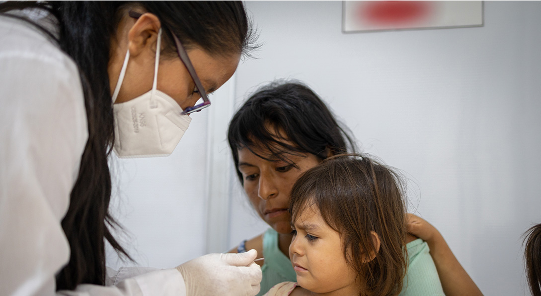 A young girl looks with confusion at her finger while a female doctor takes a blood sample.