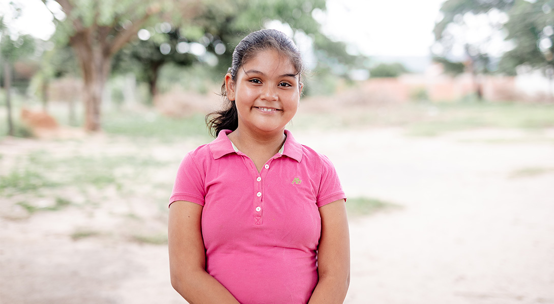 A young girl wearing a bright pink polo stands and smiles for the camera.