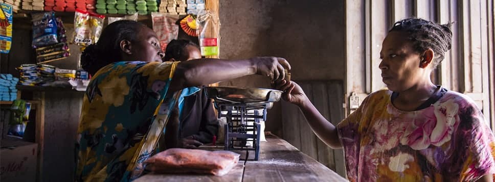 Two women at a counter of a small store exchanging money.