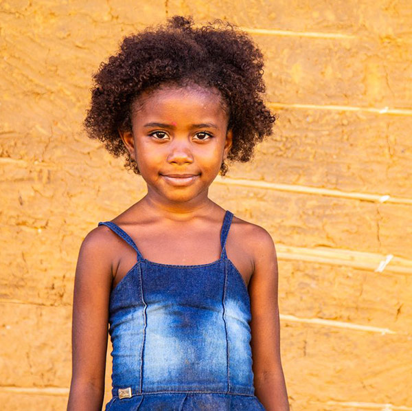 a girl in a blue dress stands in front of a yellow wall