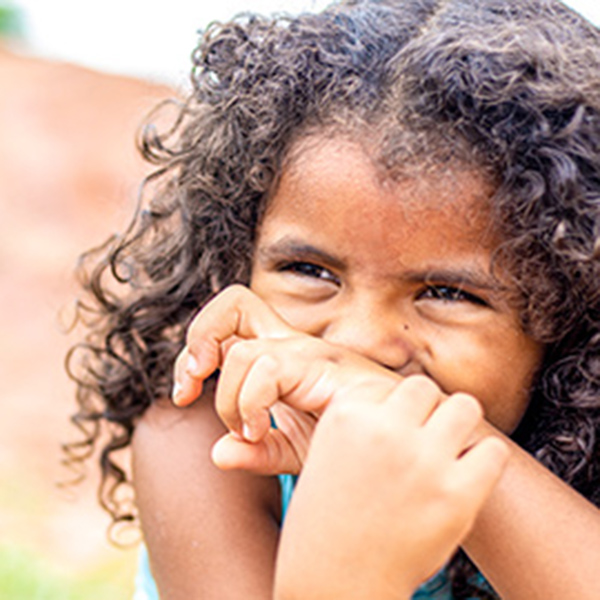 A young girl with curly hair covers her mouth with her wrist as she laughs