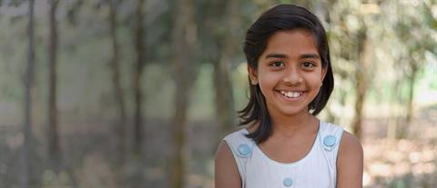 A smiling girl stands in front of a copse of trees