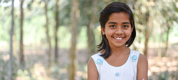 A smiling girl stands in front of a copse of trees