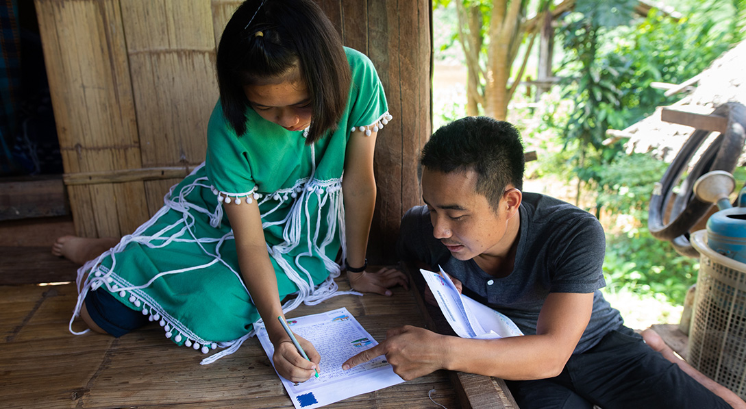 girl writes letter while Wichean assists