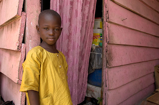 A young girl in a gold top stands outside of a pink house