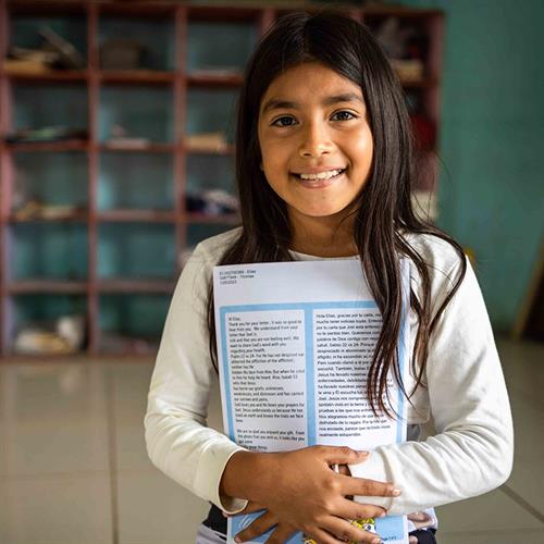 A young girl smiles and holds her sponsor letters close to her chest