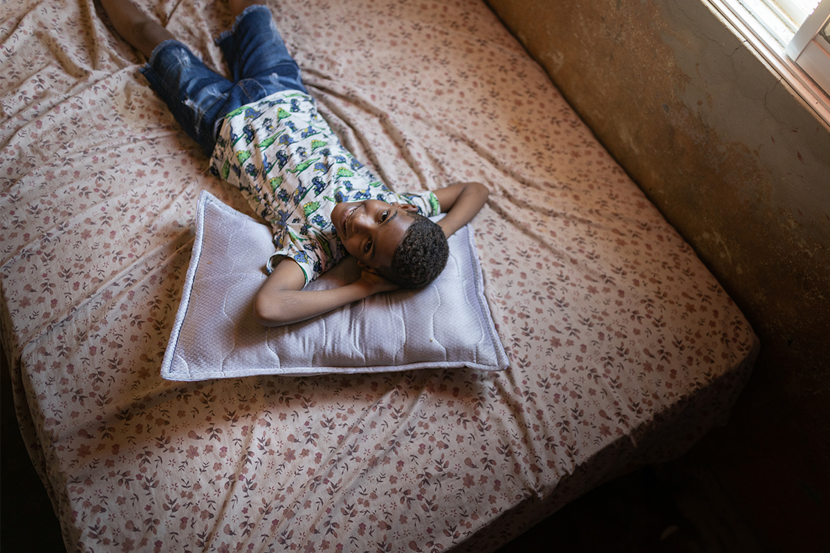 A young girl and her mother sit on a bed reading a Bible. The Bible is reflecting light on the young girl’s face as they learn about Christian values together.