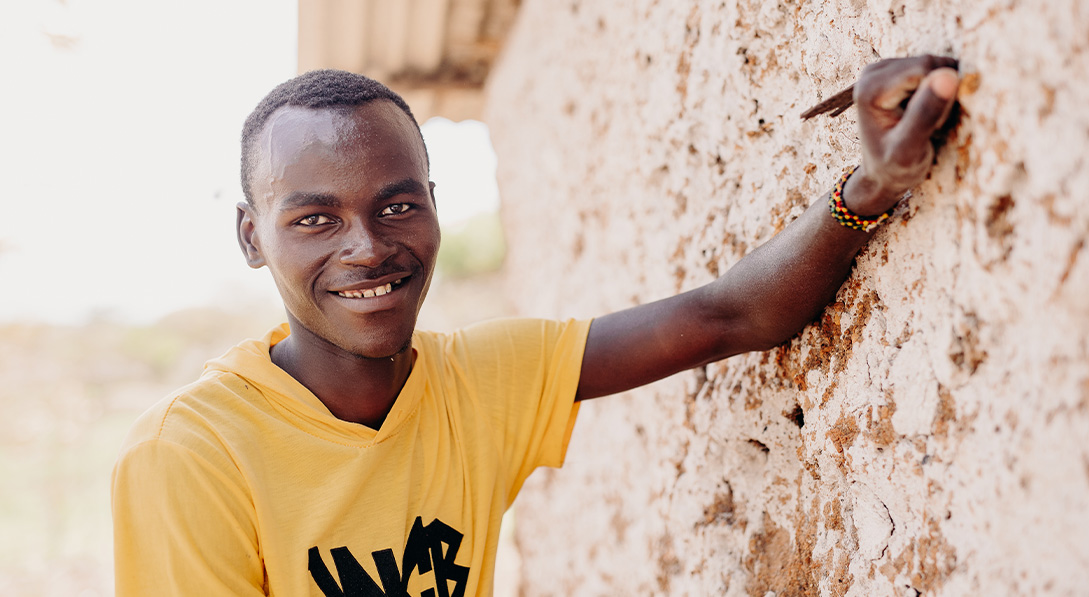 Maisha leans again a brick wall and smiles for the camera.