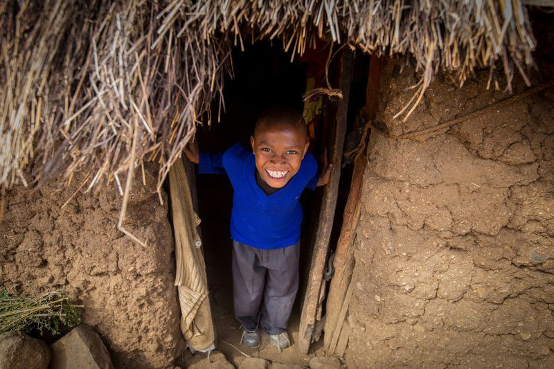 A boy looks out of his front door and smiles