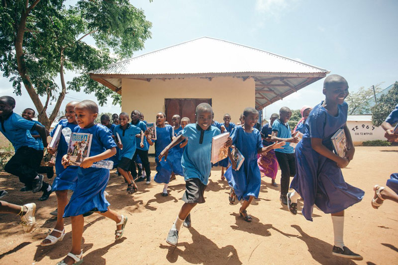 Children in unifroms run out of their center smiling