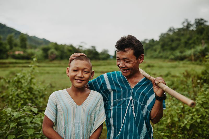 A proud father stands next to his son in a green field