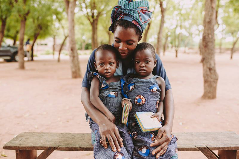 A mother holds her twin toddlers outside the child development center