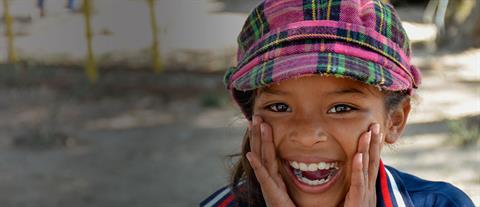 A girl wearing a plaid hat cups her hands by her mouth