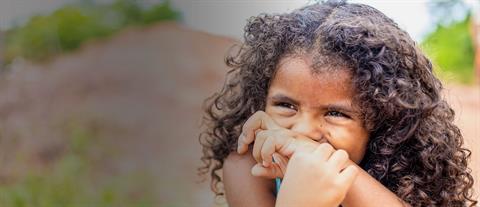 A young girl with curly hair covers her mouth with her wrist as she laughs