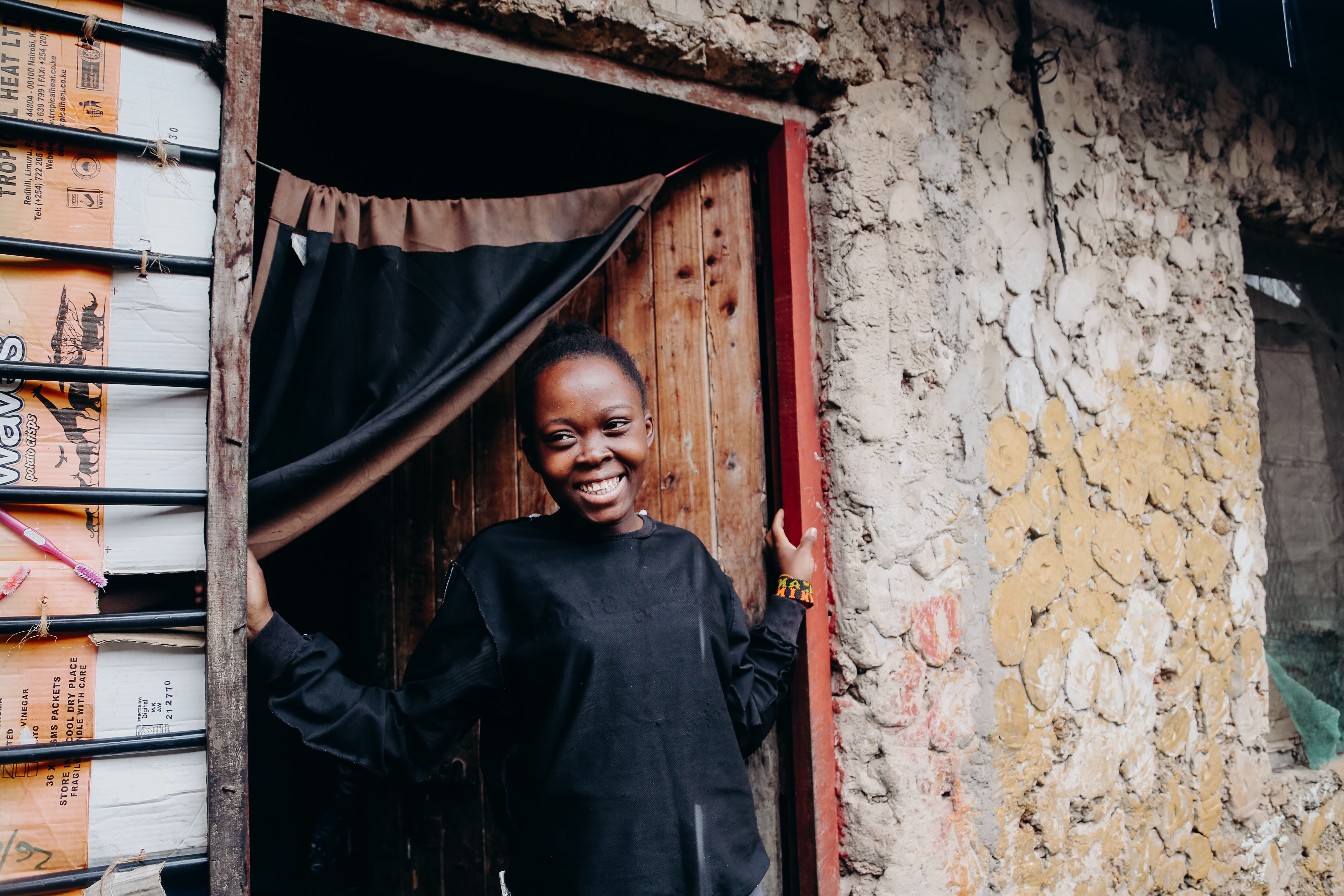 Alice is standing in a wooden doorway, with her hands on each side of the doorposts. She is wearing a black shirt. She is smiling.