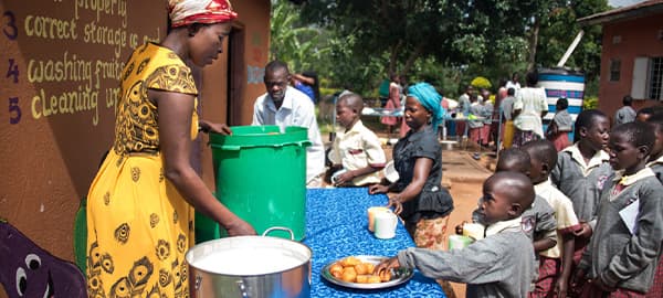 Children standing in line to receive food from a woman at a table.