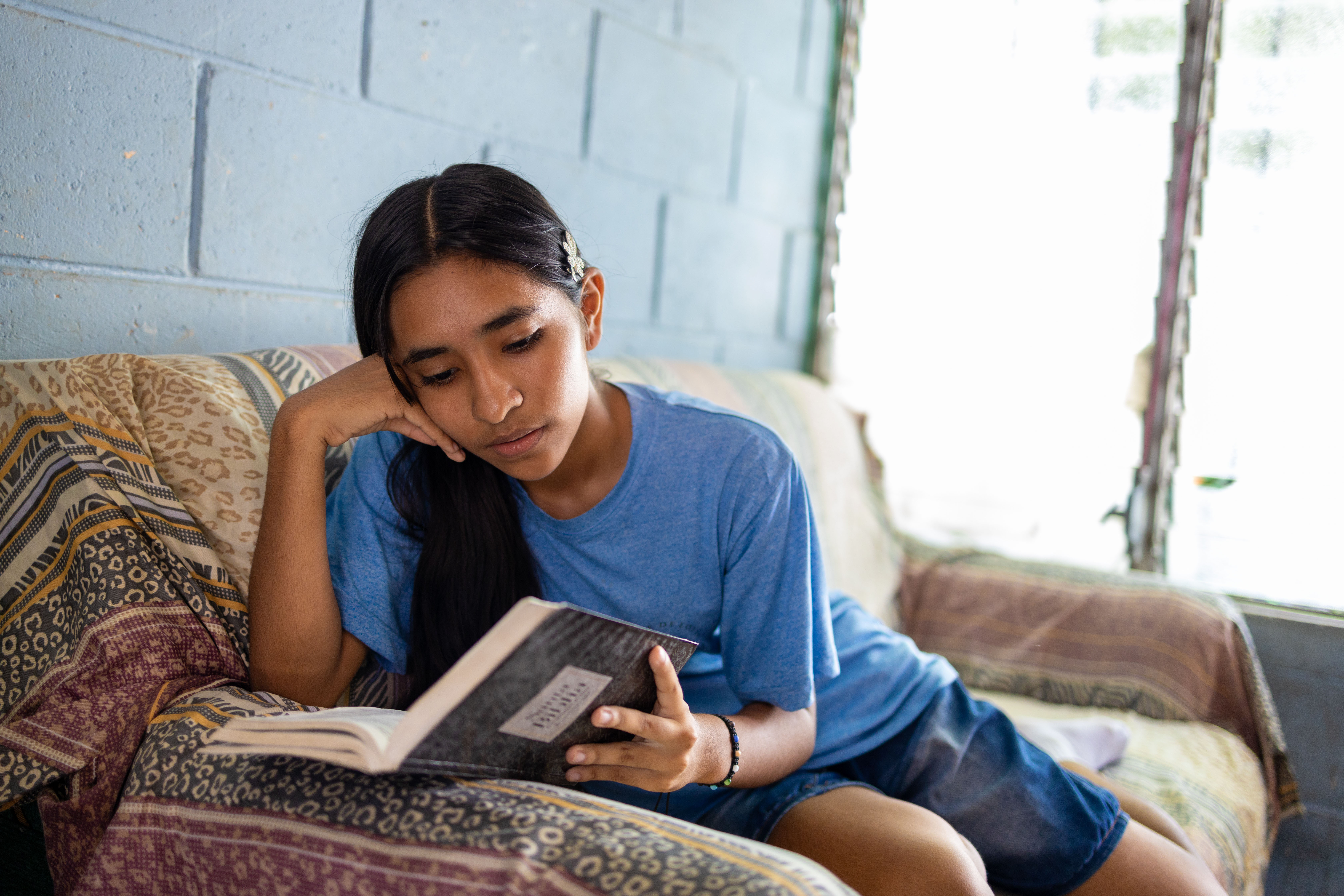 Young girl lies on her couch while reading her Bible.