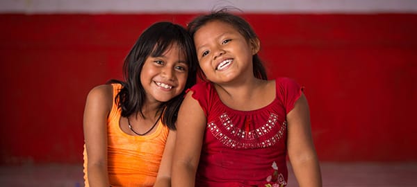 Two young girls smiling and sitting next to each other.