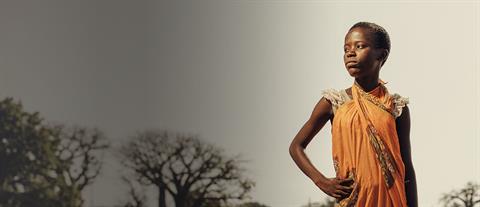 An African girl with a serious expression stands with a hand on her hip