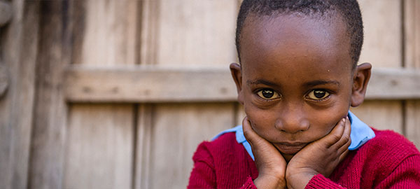 A young boy in a red sweater rests his chin in his hands