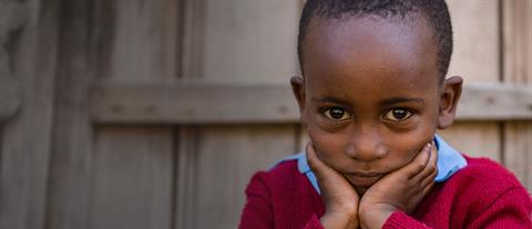 A young boy in a red sweater rests his chin in his hands