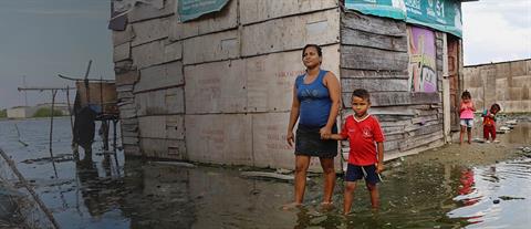 A woman and boy hold hands as they walk through ankle-deep water outside their home