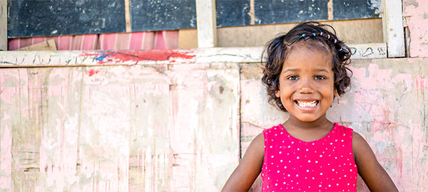 A young girl in a majenta top stands in front of a pink building