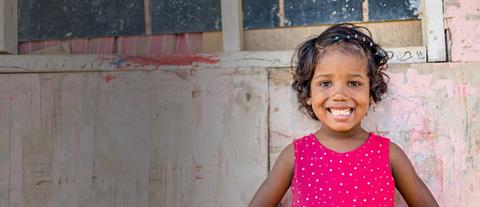 A young girl in a majenta top stands in front of a pink building