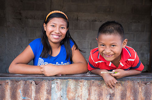 A smiling boy and girl lean over a wall