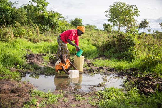 Young girl helping her mom fill plastic containers with water