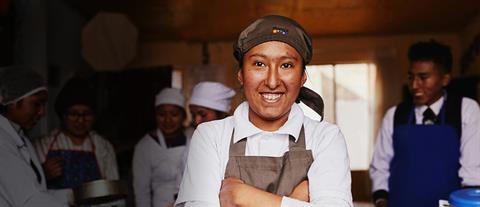 A young woman in a brown apron has her arms crossed and her hands tucked into her armpits